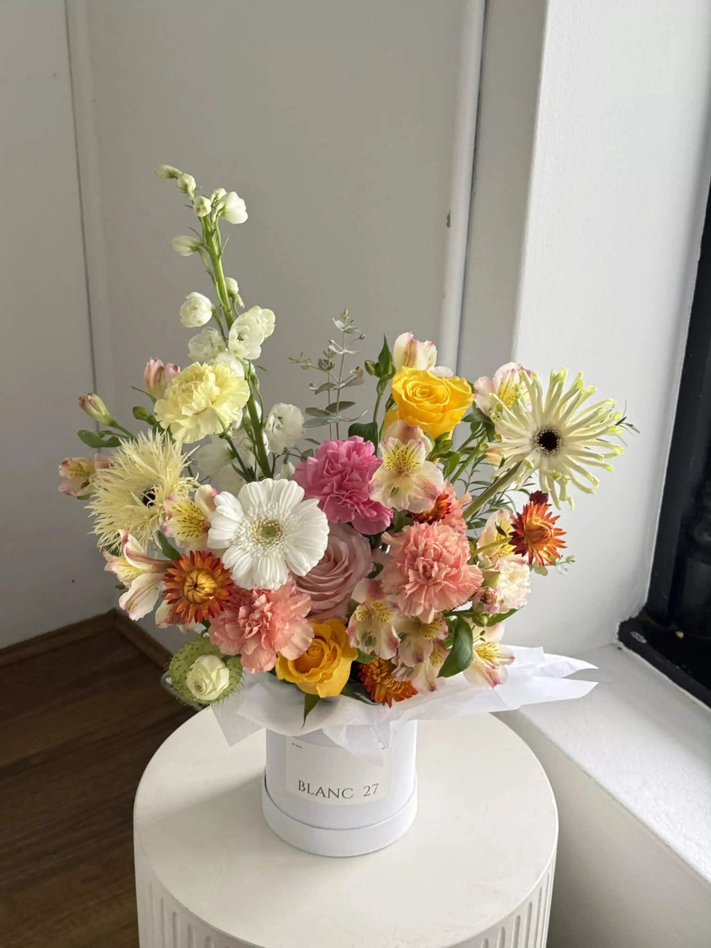 Bouquet of colorful flowers with a white container labeled 'Bancroft' on a neutral background.